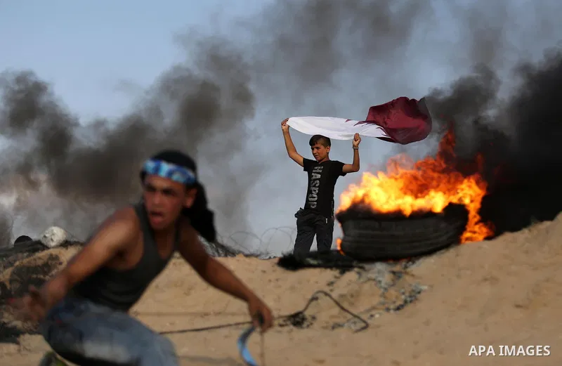 A Palestinian protester waves a Qatar flag during clashes with Israeli security forces near the border between Israel and Central Gaza Strip July 7, 2017. Photo by Ashraf Amra