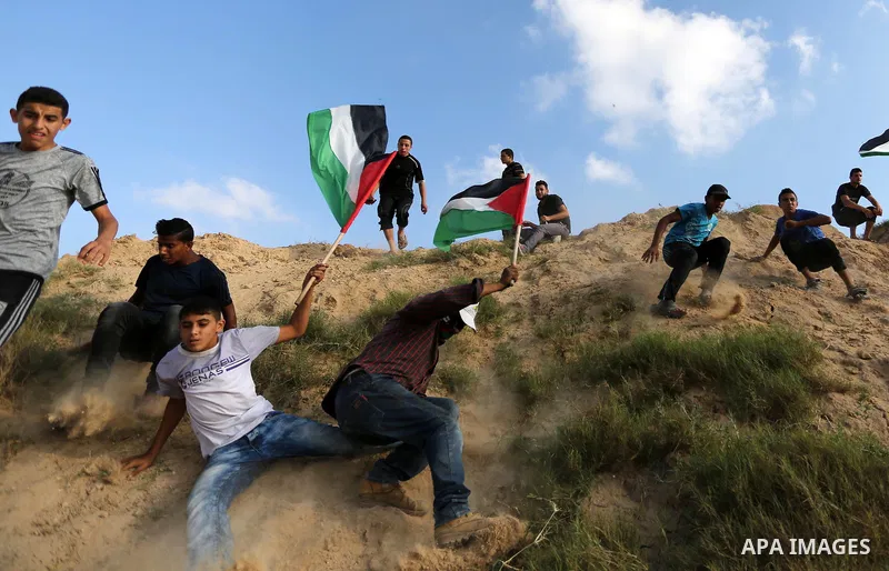 Palestinian protesters wave Palestine flags during clashes with Israeli security forces near the border between Israel and Central Gaza Strip July 7, 2017. Photo by Ashraf Amra