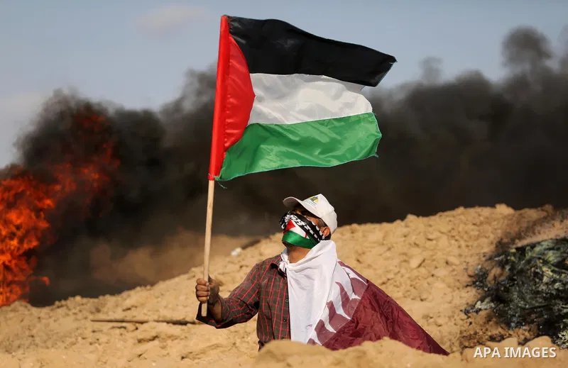 A Palestinian protester wears a Qatar flag and waves the national flag during clashes with Israeli security forces near the border between Israel and Central Gaza Strip July 7, 2017. Photo by Ashraf Amra