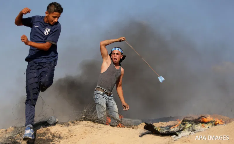 A Palestinian protester uses a slingshot to hurl stones towards Israeli security forces during clashes near the border between Israel and Central Gaza Strip July 7, 2017. Photo by Ashraf Amra