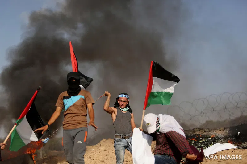 Palestinian protesters wave the national flag during clashes with Israeli security forces near the border between Israel and Central Gaza Strip July 7, 2017. Photo by Ashraf Amra