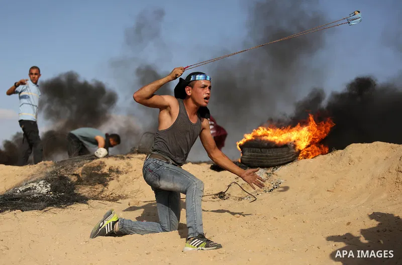 A Palestinian protester uses a slingshot to hurl stones towards Israeli security forces during clashes near the border between Israel and Central Gaza Strip July 7, 2017. Photo by Ashraf Amra