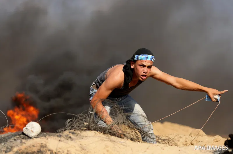 A Palestinian protester uses a slingshot to hurl stones towards Israeli security forces during clashes near the border between Israel and Central Gaza Strip July 7, 2017. Photo by Ashraf Amra