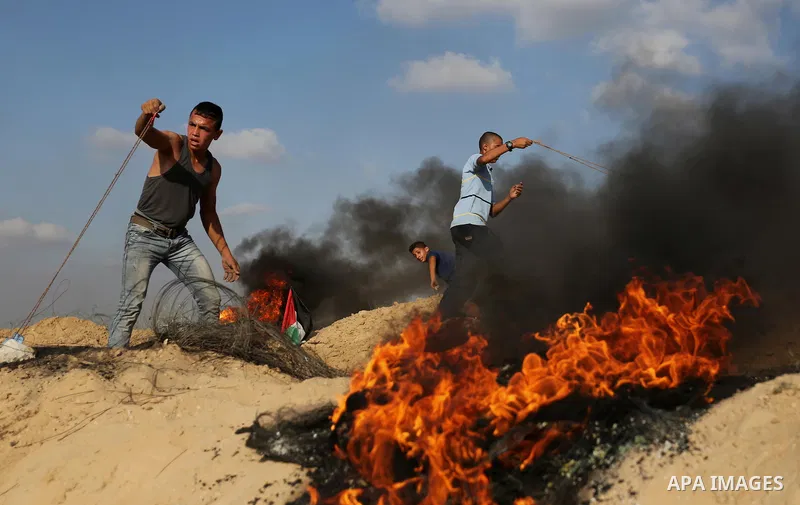 Palestinian protesters use slingshot to hurl stones towards Israeli security forces during clashes near the border between Israel and Central Gaza Strip July 7, 2017. Photo by Ashraf Amra