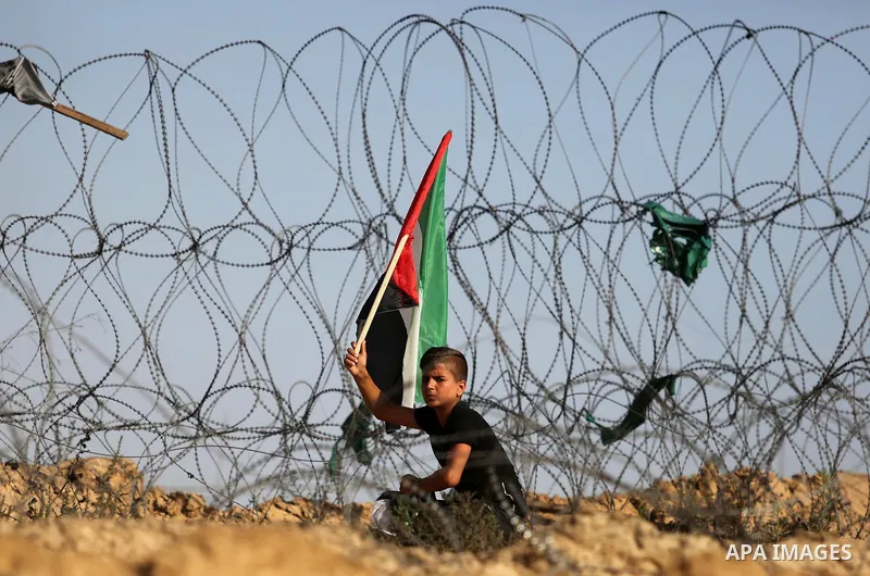 A Palestinian protester waves the national flag during clashes with Israeli security forces near the border between Israel and Central Gaza Strip July 7, 2017. Photo by Ashraf Amra