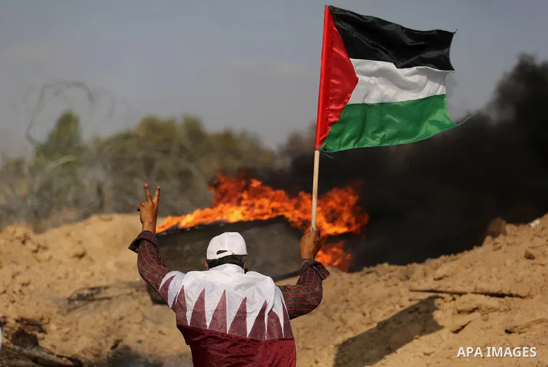 A Palestinian protester wears a Qatar flag and waves the national flag during clashes with Israeli security forces near the border between Israel and Central Gaza Strip July 7, 2017. Photo by Ashraf Amra