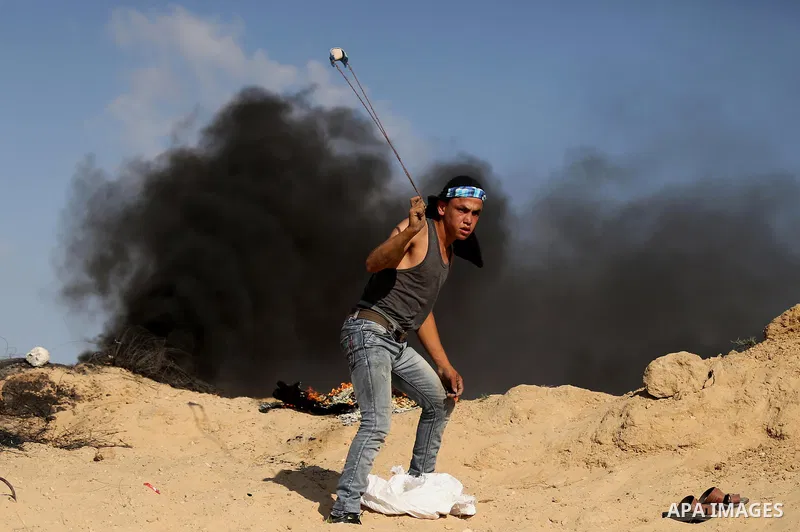 A Palestinian protester uses a slingshot to hurl stones towards Israeli security forces during clashes near the border between Israel and Central Gaza Strip July 7, 2017. Photo by Ashraf Amra