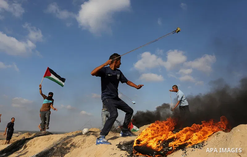 A Palestinian protester uses a slingshot to hurl stones towards Israeli security forces during clashes near the border between Israel and Central Gaza Strip July 7, 2017. Photo by Ashraf Amra