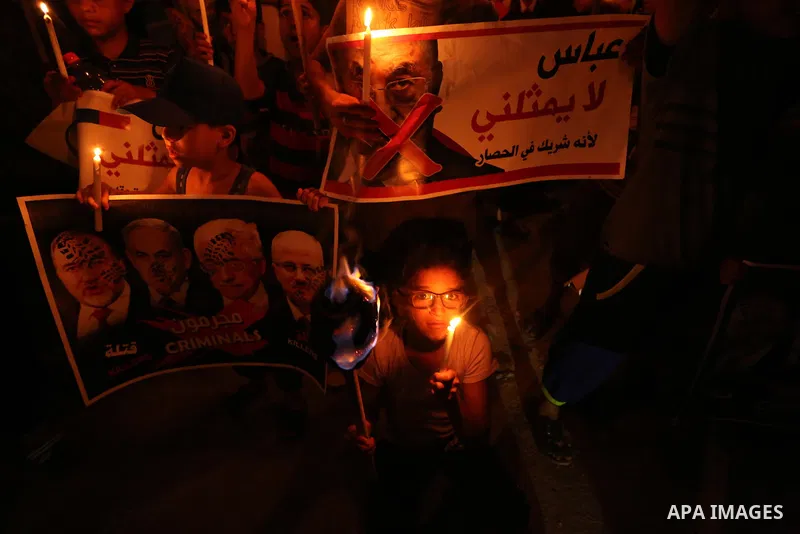 Palestinian boys hold candles during a protest against the blockade on Gaza, in Khan Younis in the southern Gaza Strip July 14, 2017. The poster (back) reads, "Abbas (Palestinian president) does not represent me because...