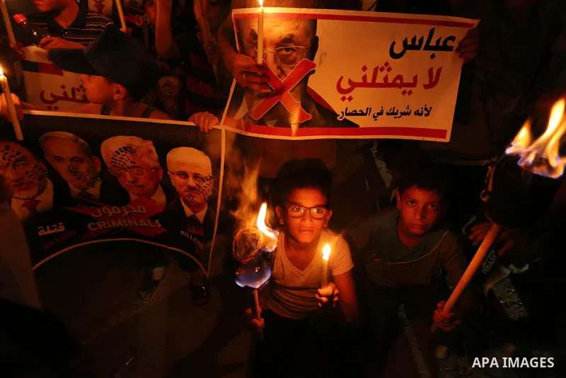 Palestinian boys hold candles during a protest against the blockade on Gaza, in Khan Younis in the southern Gaza Strip July 14, 2017. The poster (back) reads, "Abbas (Palestinian president) does not represent me because...