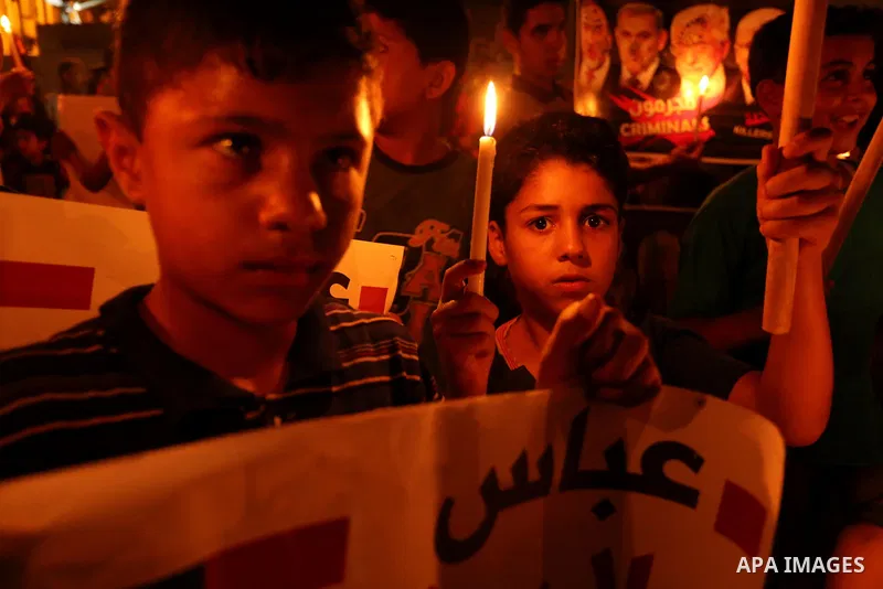 Palestinian boys hold candles and posters during a protest against the blockade on Gaza, in Khan Younis in the southern Gaza Strip July 14, 2017. The poster (back) reads, "Abbas (Palestinian president) does not represent...
