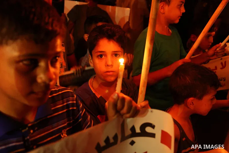 Palestinian boys hold candles and posters during a protest against the blockade on Gaza, in Khan Younis in the southern Gaza Strip July 14, 2017. The poster (back) reads, "Abbas (Palestinian president) does not represent...