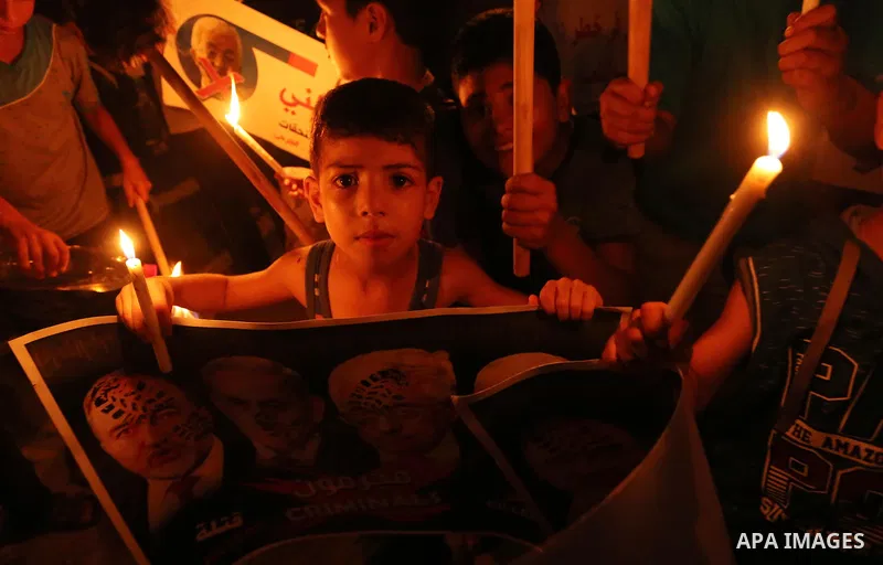 Palestinian boys hold candles and posters during a protest against the blockade on Gaza, in Khan Younis in the southern Gaza Strip July 14, 2017. The poster (back) reads, "Abbas (Palestinian president) does not represent...