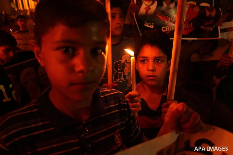 Palestinian boys hold candles and posters during a protest against the blockade on Gaza, in Khan Younis in the southern Gaza Strip July 14, 2017. The poster (back) reads, "Abbas (Palestinian president) does not represent...