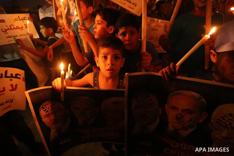 Palestinian boys hold candles and posters during a protest against the blockade on Gaza, in Khan Younis in the southern Gaza Strip July 14, 2017. The poster (back) reads, "Abbas (Palestinian president) does not represent...