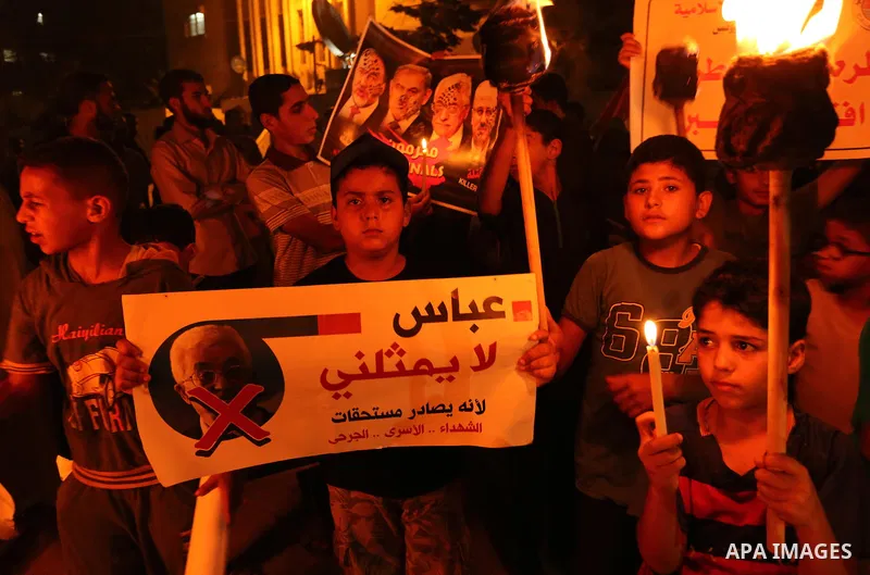 Palestinian boys hold candles during a protest against the blockade on Gaza, in Khan Younis in the southern Gaza Strip July 14, 2017. The poster (back) reads, "Abbas (Palestinian president) does not represent me because...