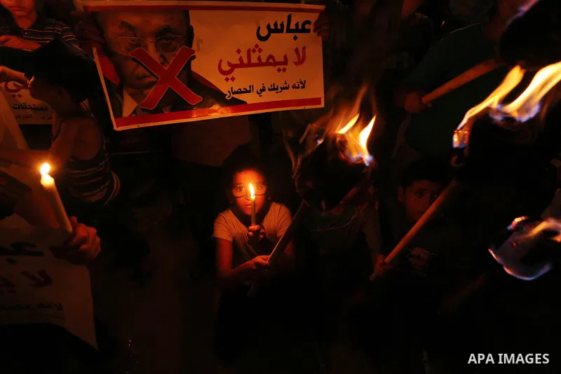 Palestinian boys hold candles during a protest against the blockade on Gaza, in Khan Younis in the southern Gaza Strip July 14, 2017. The poster (back) reads, "Abbas (Palestinian president) does not represent me because...