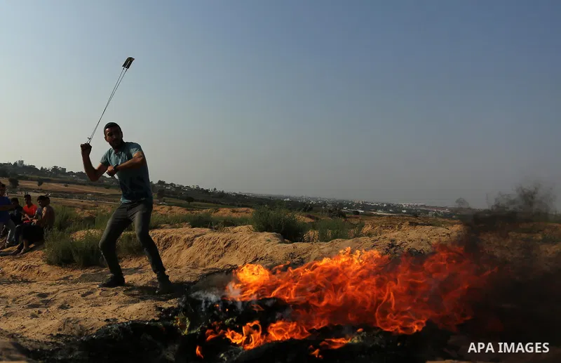 A Palestinian protester uses a slingshot to hurl stones towards Israeli security forces during clashes near the border between Israel and central Gaza Strip in a protest against Israel's new security measures at the entr...