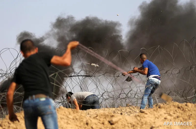 Palestinian protesters use a slingshots to hurl stones towards Israeli security forces during clashes near the border between Israel and central Gaza Strip in a protest against Israel's new security measures at the entra...