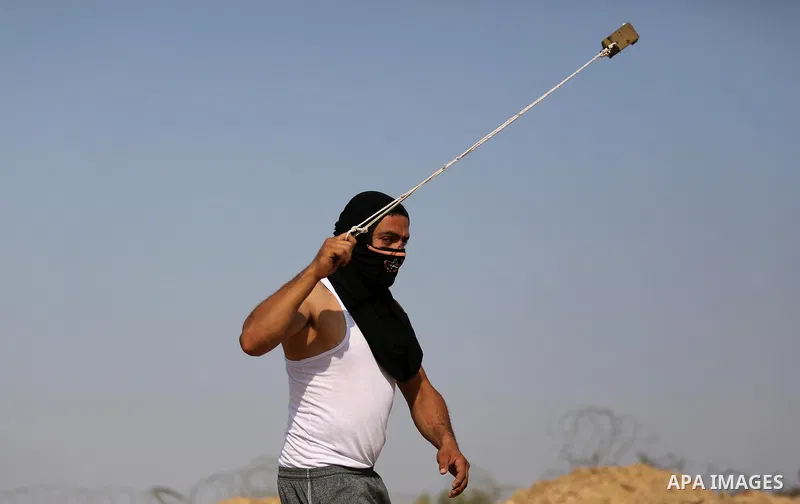 A Palestinian protester uses a slingshot to hurl stones towards Israeli security forces during clashes near the border between Israel and central Gaza Strip in a protest against Israel's new security measures at the entr...