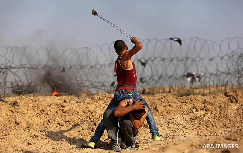 A Palestinian protester uses a slingshot to hurl stones towards Israeli security forces during clashes near the border between Israel and central Gaza Strip in a protest against Israel's new security measures at the entr...