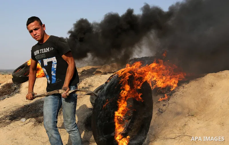 A Palestinian protester burns tires during clashes with Israeli security forces near the border between Israel and central Gaza Strip in a protest against Israel's new security measures at the entrance to the al-Aqsa mos...