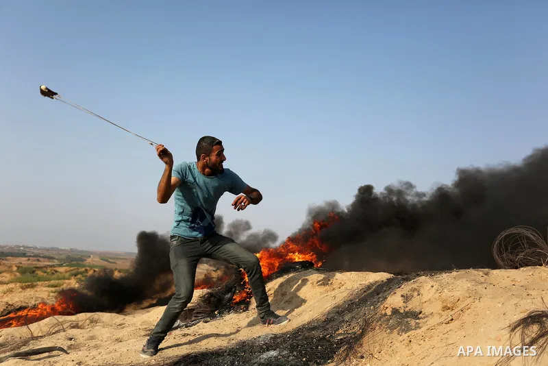A Palestinian protester uses a slingshot to hurl stones towards Israeli security forces during clashes near the border between Israel and central Gaza Strip in a protest against Israel's new security measures at the entr...