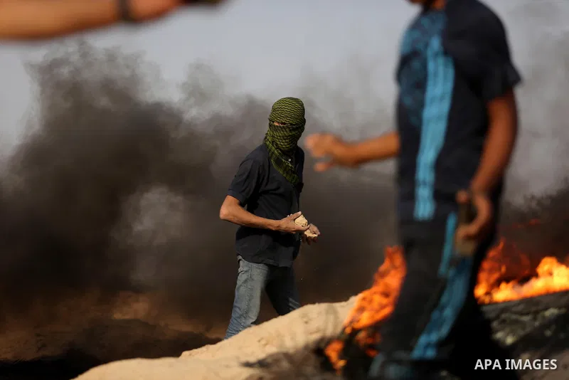 A Palestinian protester hurls stones towards Israeli security forces during clashes near the border between Israel and central Gaza Strip in a protest against Israel's new security measures at the entrance to the al-Aqsa...