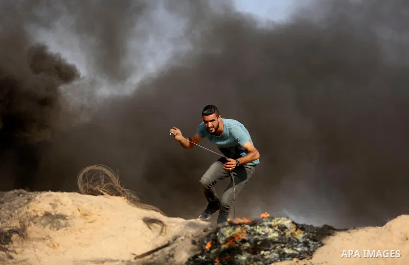 A Palestinian protester uses a slingshot to hurl stones towards Israeli security forces during clashes near the border between Israel and central Gaza Strip in a protest against Israel's new security measures at the entr...