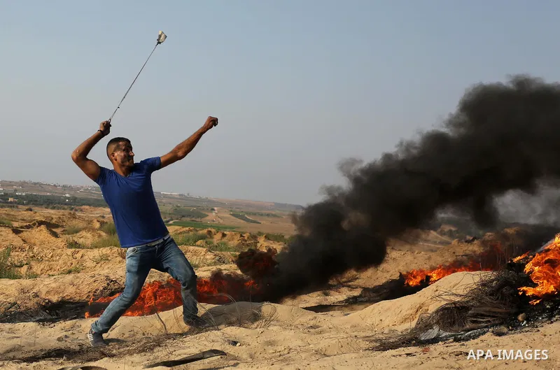A Palestinian protester uses a slingshot to hurl stones towards Israeli security forces during clashes near the border between Israel and central Gaza Strip in a protest against Israel's new security measures at the entr...