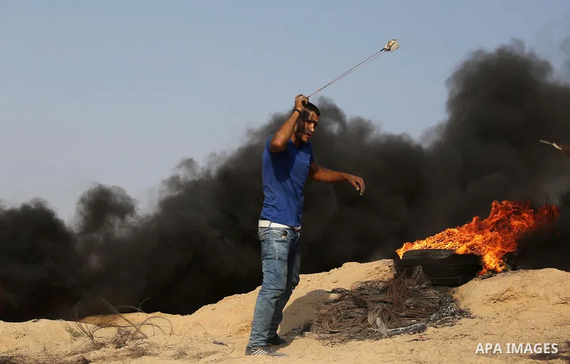 A Palestinian protester uses a slingshot to hurl stones towards Israeli security forces during clashes near the border between Israel and central Gaza Strip in a protest against Israel's new security measures at the entr...