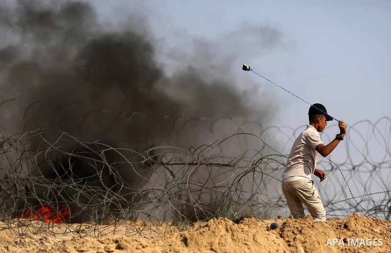 A Palestinian protester uses a slingshot to hurl stones towards Israeli security forces during clashes near the border between Israel and central Gaza Strip in a protest against Israel's new security measures at the entr...
