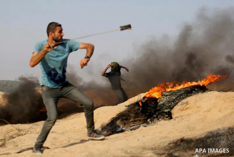 A Palestinian protester hurls stones towards Israeli security forces during clashes near the border between Israel and central Gaza Strip in a protest against Israel's new security measures at the entrance to the al-Aqsa...