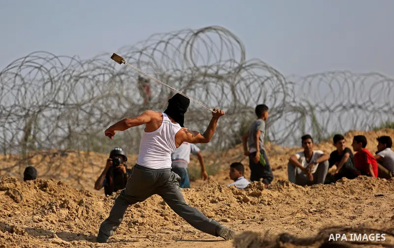 A Palestinian protester uses a slingshot to hurl stones towards Israeli security forces during clashes near the border between Israel and central Gaza Strip in a protest against Israel's new security measures at the entr...