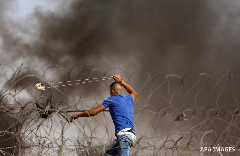 A Palestinian protester uses a slingshot to hurl stones towards Israeli security forces during clashes near the border between Israel and central Gaza Strip in a protest against Israel's new security measures at the entr...