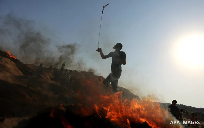A Palestinian protester uses a slingshot to hurl stones towards Israeli security forces during clashes near the border between Israel and central Gaza Strip in a protest against Israel's new security measures at the entr...