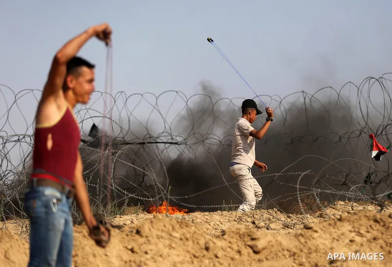 A Palestinian protester uses a slingshot to hurl stones towards Israeli security forces during clashes near the border between Israel and central Gaza Strip in a protest against Israel's new security measures at the entr...