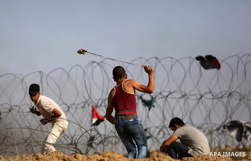 A Palestinian protester uses a slingshot to hurl stones towards Israeli security forces during clashes near the border between Israel and central Gaza Strip in a protest against Israel's new security measures at the entr...