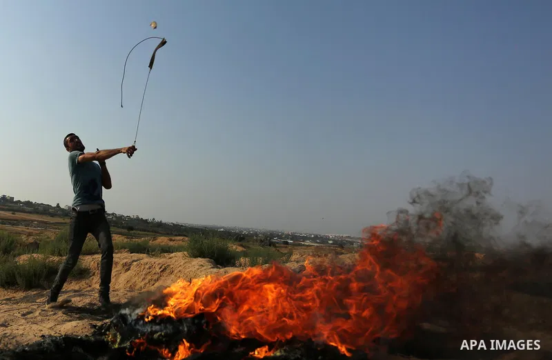A Palestinian protester uses a slingshot to hurl stones towards Israeli security forces during clashes near the border between Israel and central Gaza Strip in a protest against Israel's new security measures at the entr...