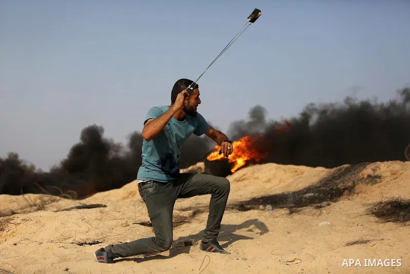 A Palestinian protester uses a slingshot to hurl stones towards Israeli security forces during clashes near the border between Israel and central Gaza Strip in a protest against Israel's new security measures at the entr...