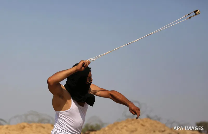 A Palestinian protester uses a slingshot to hurl stones towards Israeli security forces during clashes near the border between Israel and central Gaza Strip in a protest against Israel's new security measures at the entr...