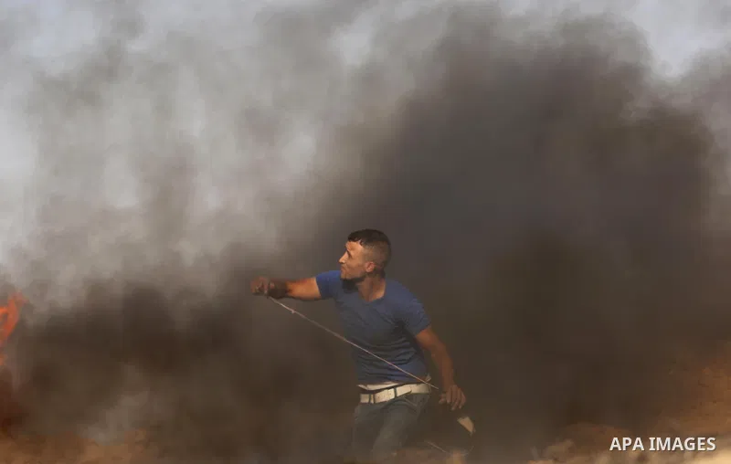 A Palestinian protester uses a slingshot to hurl stones towards Israeli security forces during clashes near the border between Israel and central Gaza Strip in a protest against Israel's new security measures at the entr...