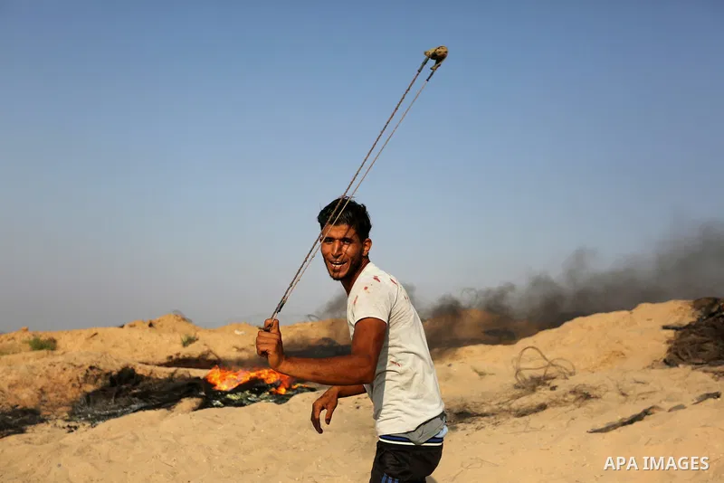 A Palestinian protester uses a slingshot to hurl stones towards Israeli security forces during clashes near the border between Israel and central Gaza Strip in a protest against Israel's new security measures at the entr...