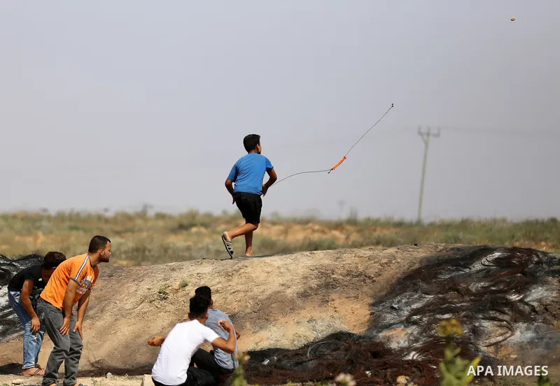 A Palestinian protester uses a slingshot to hurl stones towards Israeli security forces during clashes near the border fence east of Jabalia refugee camp in a protest against Israel's new security measures at the entranc...