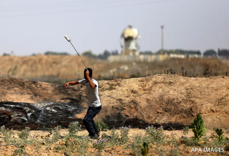 A Palestinian protester uses a slingshot to hurl stones towards Israeli security forces during clashes near the border fence east of Jabalia refugee camp in a protest against Israel's new security measures at the entranc...