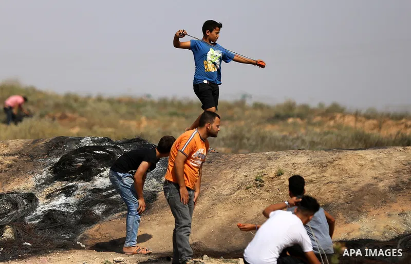 A Palestinian protester uses a slingshot to hurl stones towards Israeli security forces during clashes near the border fence east of Jabalia refugee camp in a protest against Israel's new security measures at the entranc...