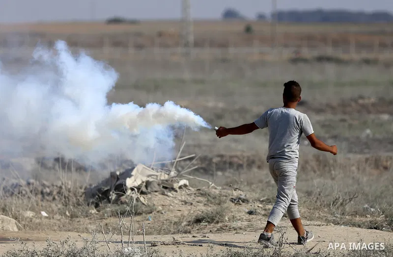 A Palestinian protester throws back a teargas canister fired by Israeli security forces during clashes near the border between Israel and eastern Gaza strip in a protest against Israel's new security measures at the entr...