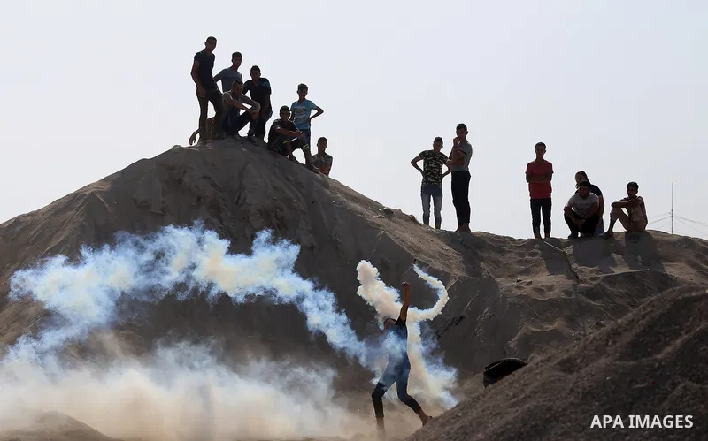 A Palestinian protester throws back a teargas canister fired by Israeli security forces during clashes near the border between Israel and eastern Gaza strip in a protest against Israel's new security measures at the entr...