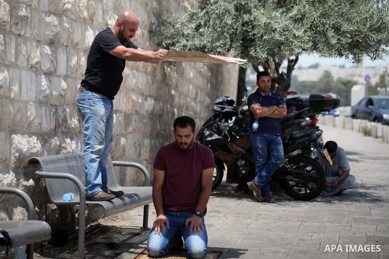 A Palestinian man uses a piece of cardboard to cover a man from the soaring heat as he pray outside the Lion's Gate a main entrance to the Al-Aqsa mosque compound in Jerusalem's Old City on July 24, 2017 as Palestinians...