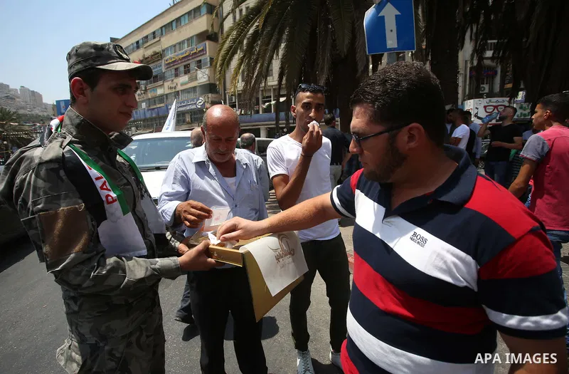 A Palestinian security man distributes sweets to people in the street, as a celebration of the victory at Al-Aqsa Mosque, in the West Bank City of Hebron, on July 27, 2017. Israel removed security apparatus from the entr...